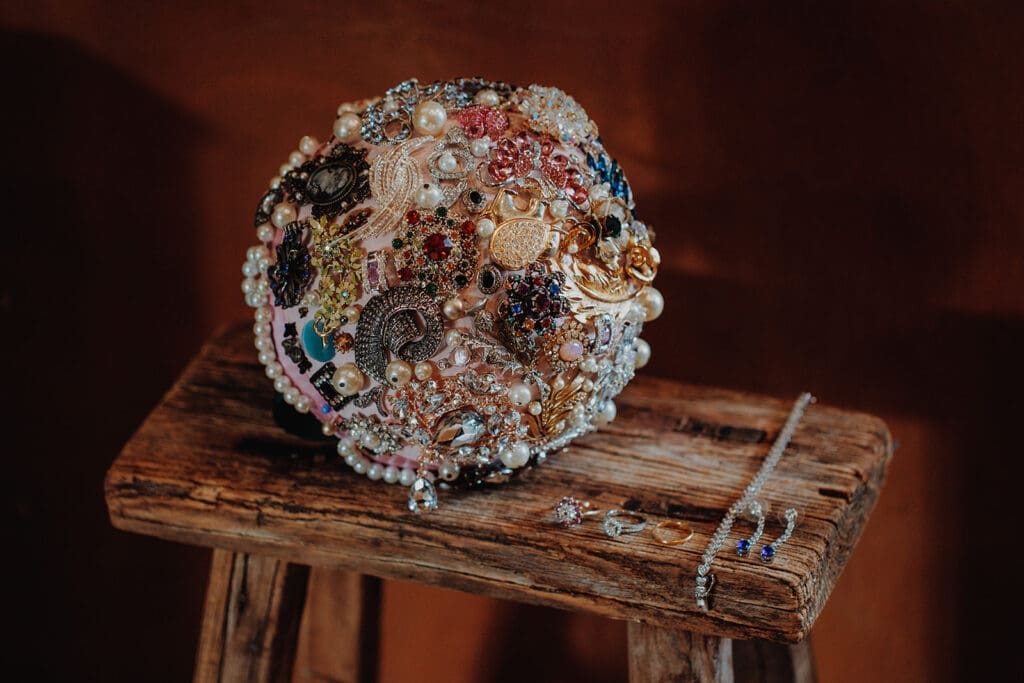 A stunning bouquet made up of vintage and antique broaches, laid on a stool next to beautiful eclectic jewellery