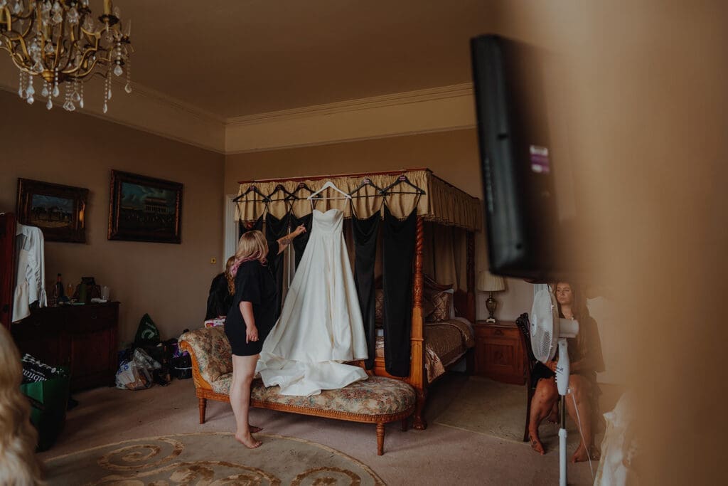 A wedding dress hung up next to her black bridesmaids dresses on a four poster bed.