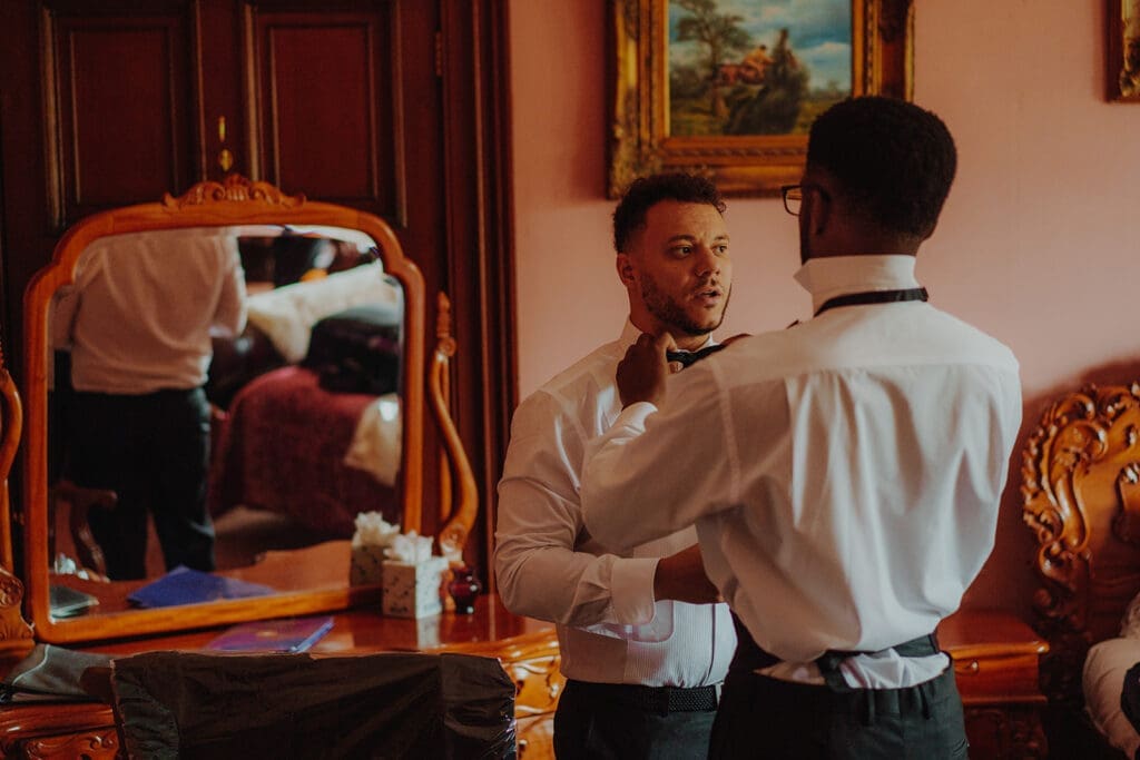 A groomsman getting his bow tie done up by another wedding party member
