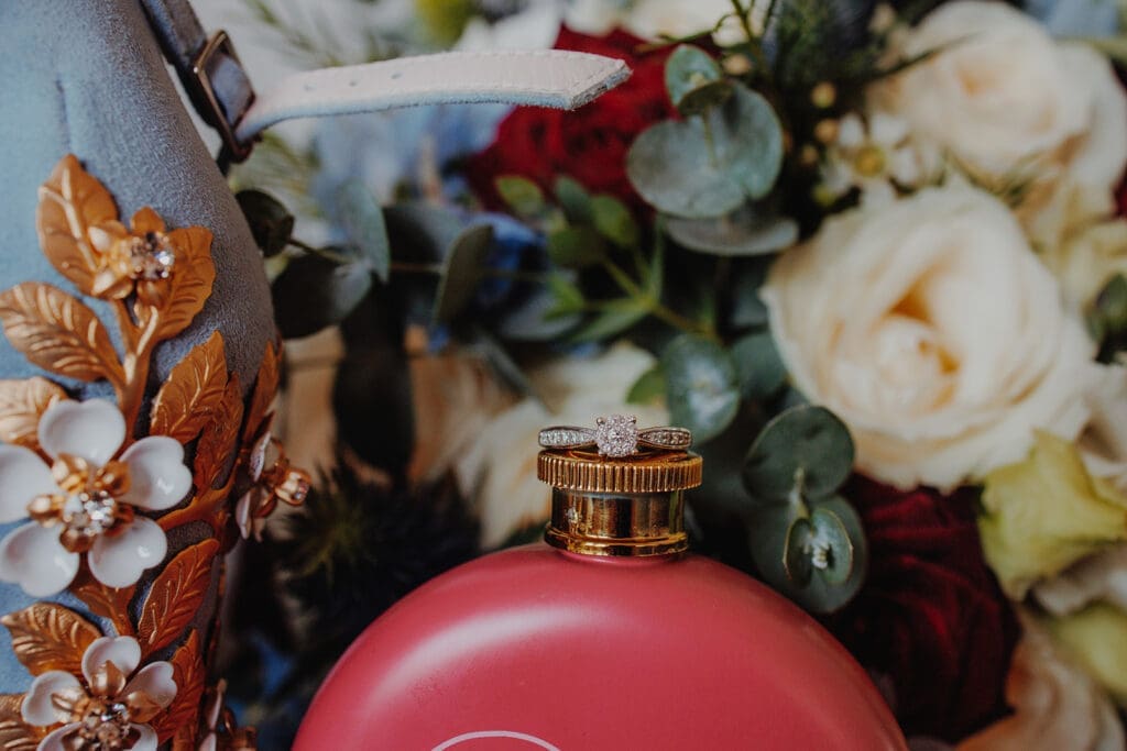 Engagement ring sitting on top of a pink flask, in front of a bouquet of flowers
