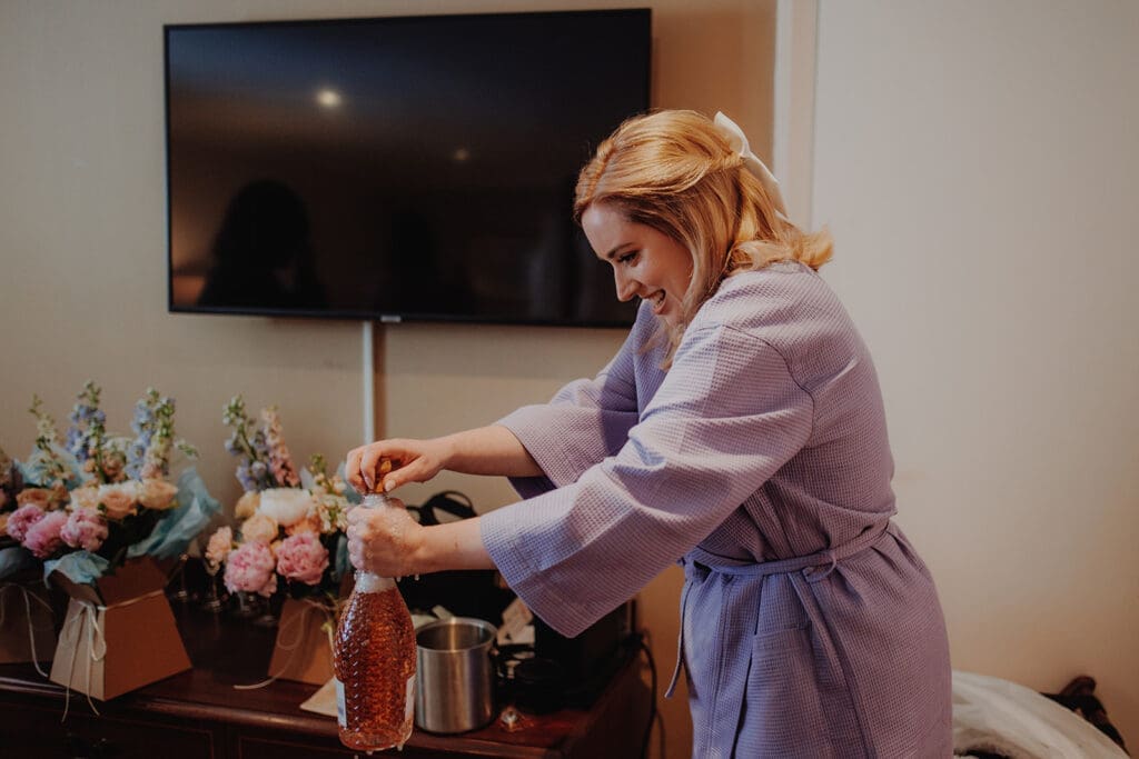 A bride to be pops open a bottle of prosecco on her wedding morning