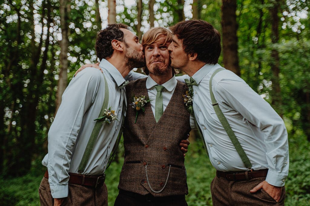 A groom with his two groomsmen, who are kissing him on each cheek!