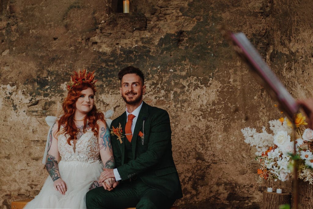 Newlyweds during their wedding ceremony. The bride wears a dried flower crown and the groom wears a forest green three piece suit