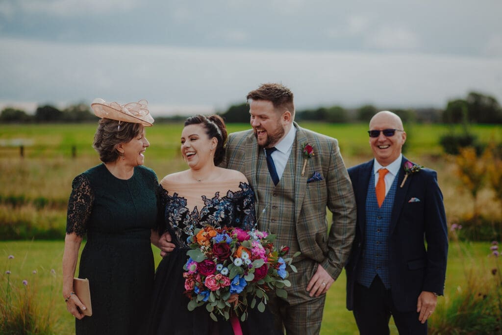 The happy couple with their parents, laughing together for a wedding group photo