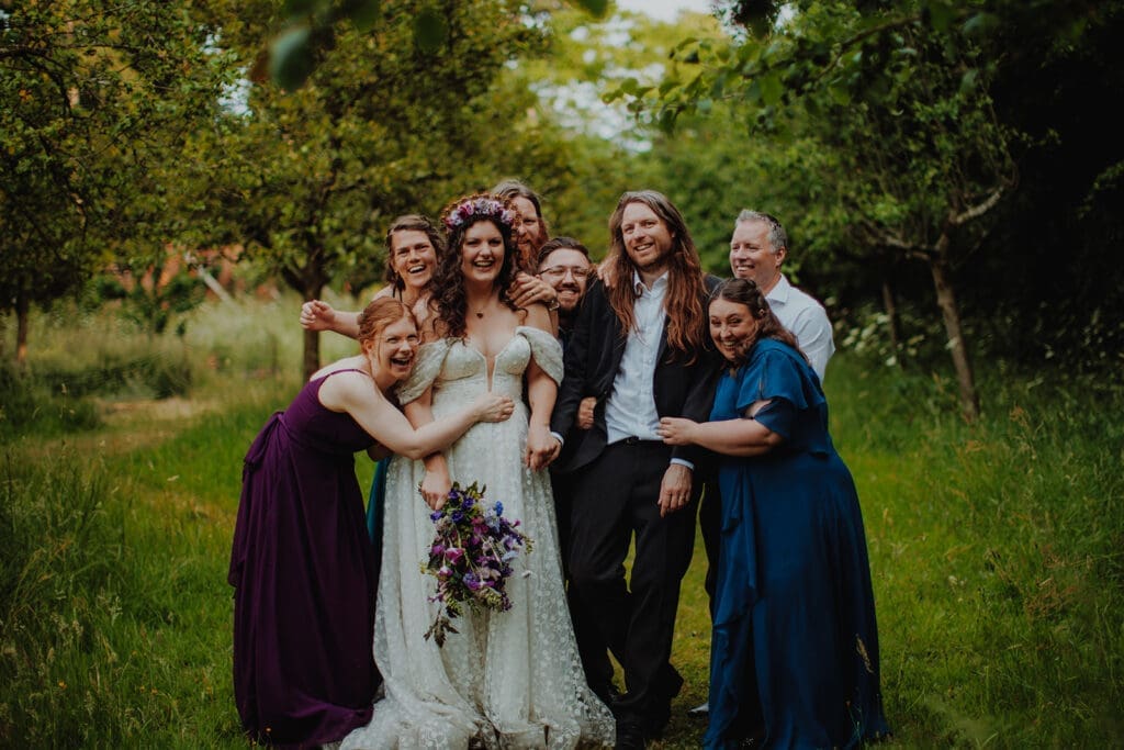 The happy couple and their friends all laugh and hug each other in the woods