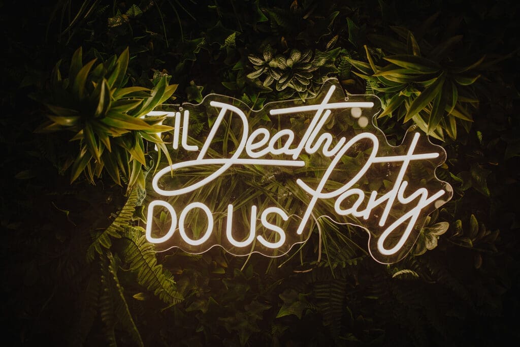 A neon sign saying Til Death Do Us Party on a green tropical backdrop