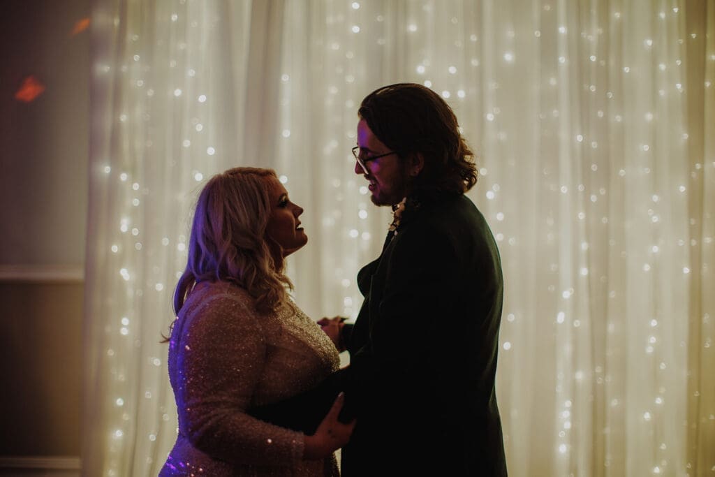 A romantic shot of newlyweds in front of a wall of fairylights. 