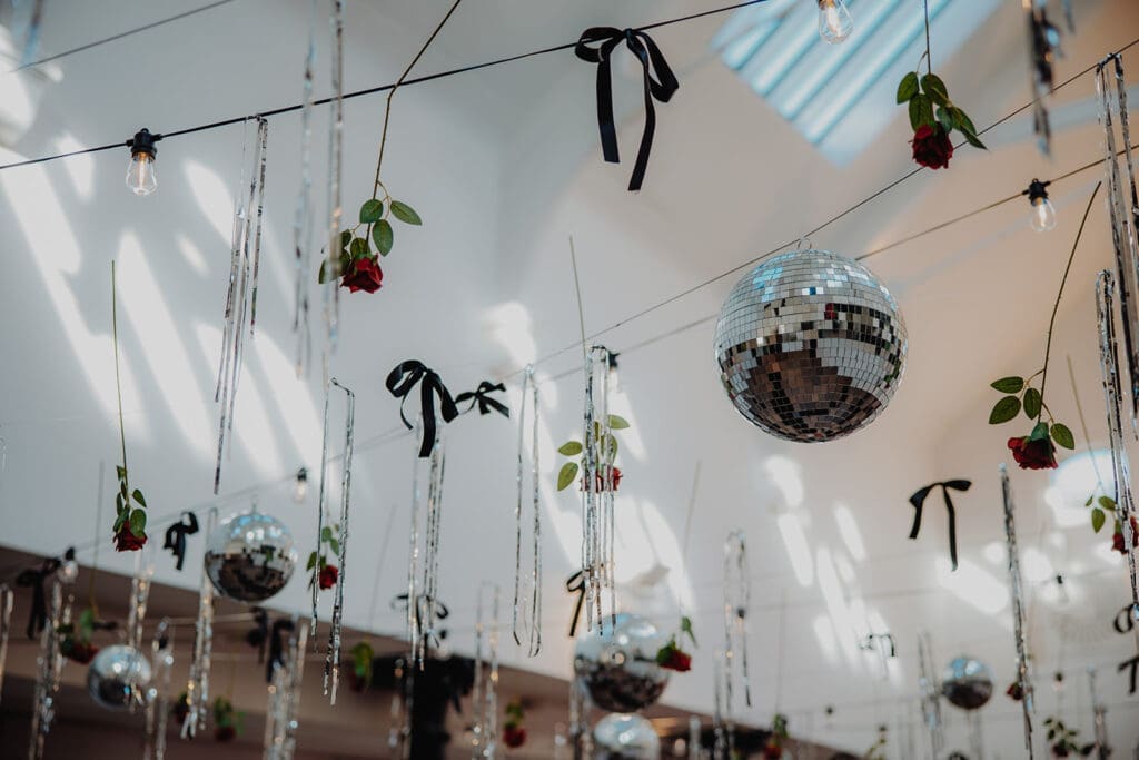 Disco balls and roses hanging from string from the ceiling in a bright open wedding venue