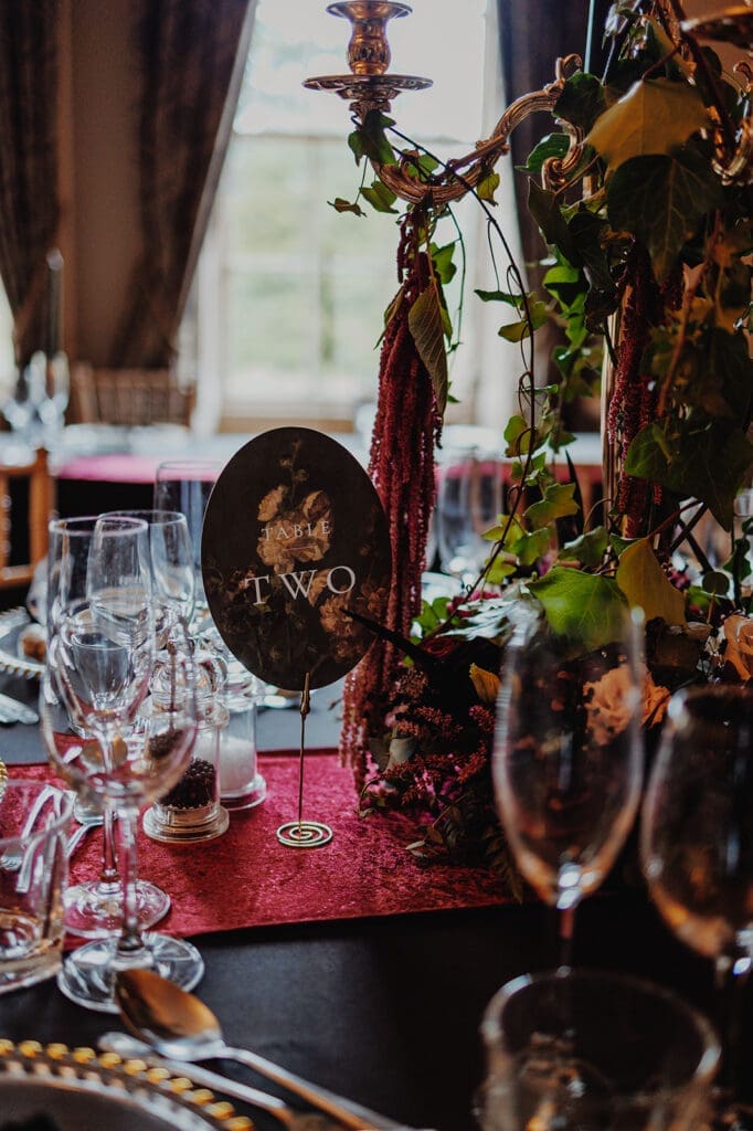 A table place setting showing opulent decor and lots of lovely glassware on a red jewel tone runner