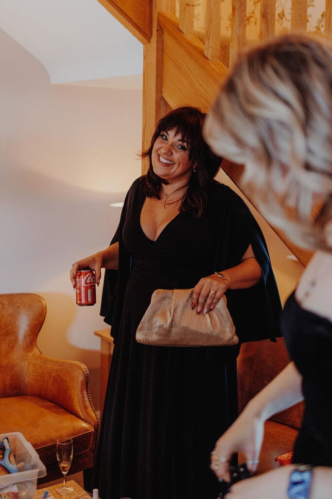 A bridesmaid laughs while holding a clutch bag and can of Coke 