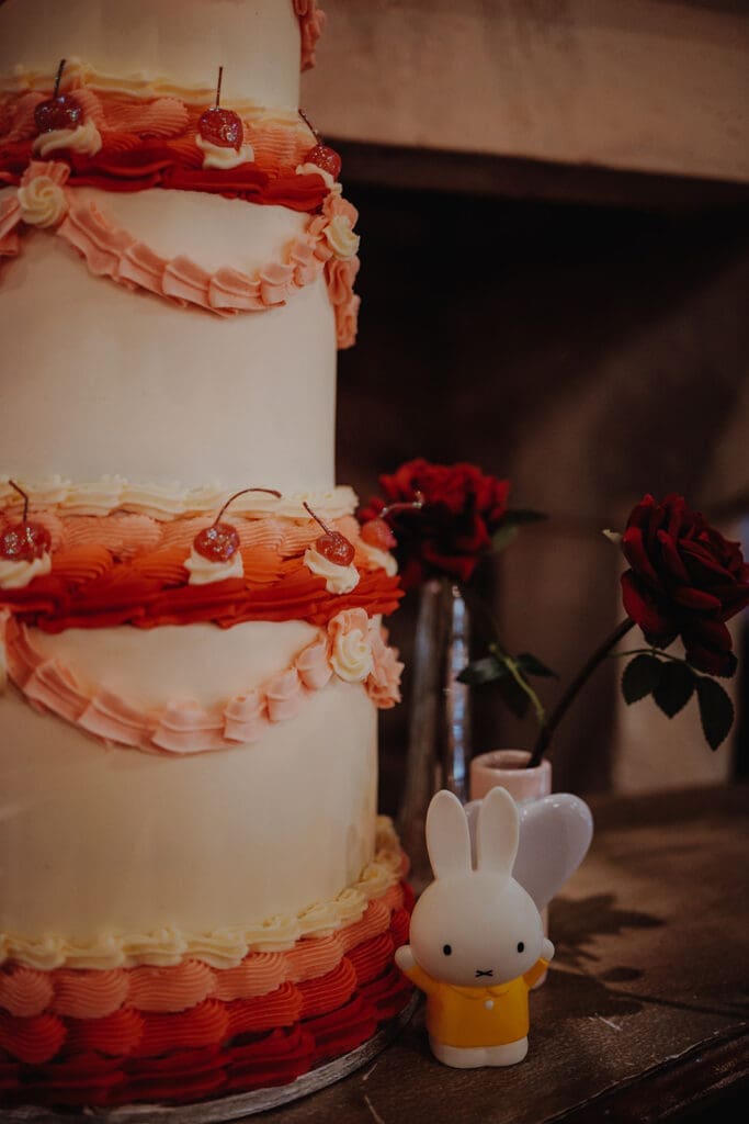 A 3 tier cake with frilly frosting in red and pink, topped with glittery cherries